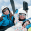Three people wearing skis and helmets are smiling.