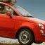 A woman driving in a red car with luggage on the roof.